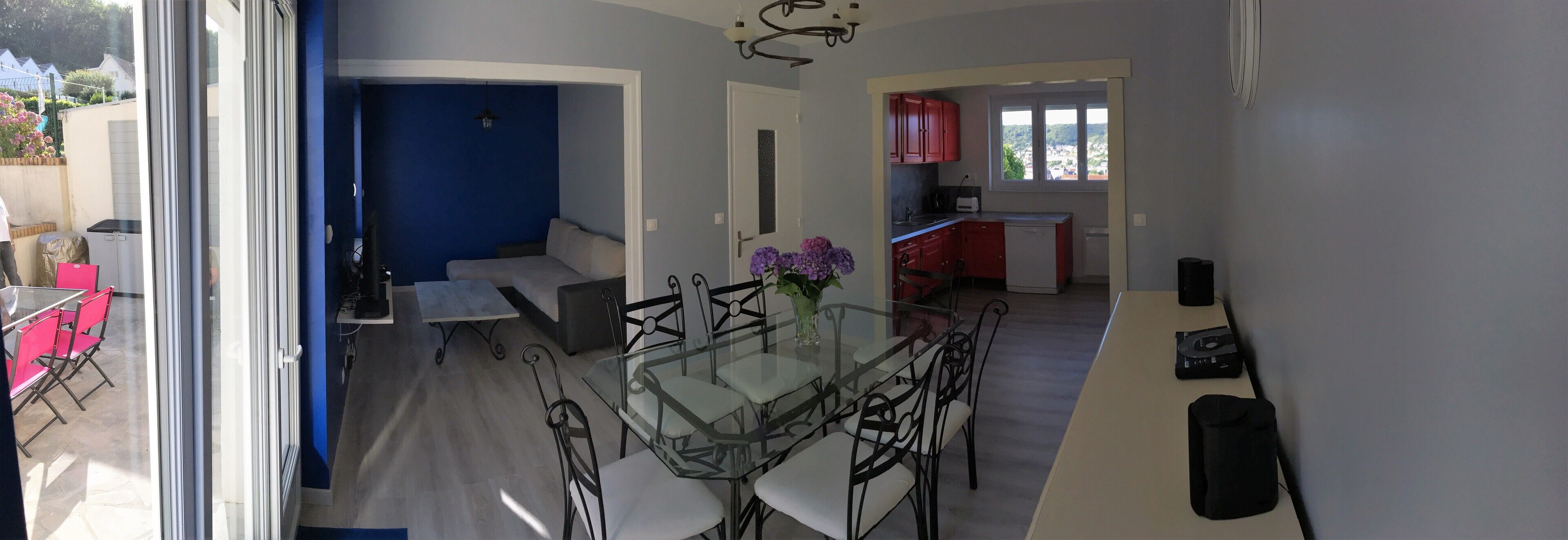 A modern kitchen with red cabinets, a dining area with a glass table and metal chairs, and a view of the outside.