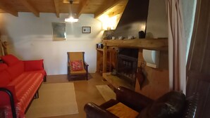 Ein gemütliches Wohnzimmer mit einem roten Sofa, einem Holzstuhl, einem Kamin und einer Holzbalkendecke.