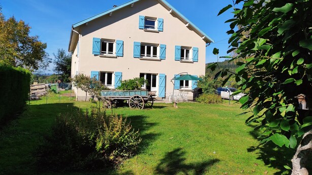 A two-story house with blue shutters, a front porch with chairs, and a garden area. - La Maison du Patrel - Bed and breakfast_4 people (Ban sur Meurthe/Clefcy)