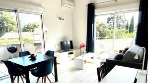 A modern living room with a dining area, large windows, and a view of the outdoors. - Apartment T2.40 m2, air-conditioned, 3 terraces, 350 m from the beach. Private parking. (Saint-Cyr-sur-Mer)