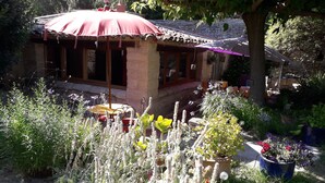 A rustic house with a red roof, surrounded by lush greenery and various plants.