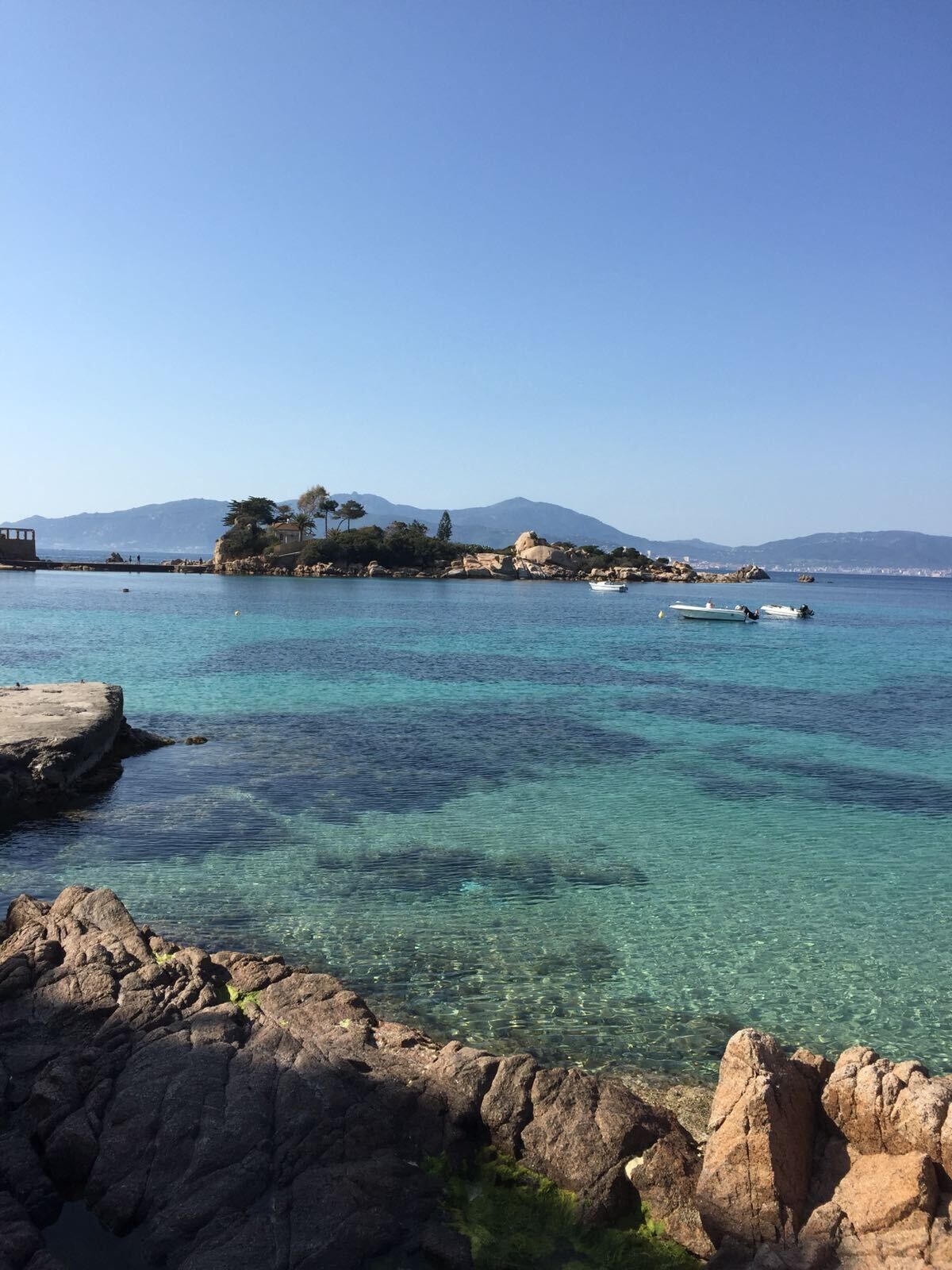 A coastal scene with clear turquoise water, rocky shorelines, and distant mountains.