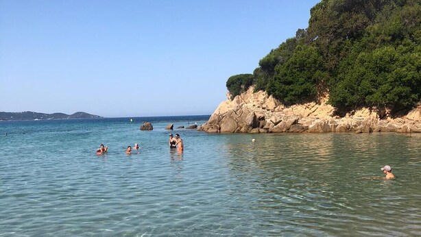 A beach with clear shallow waters, a rocky outcrop with greenery, and a distant shoreline. - Very recent 3-room apartment in PORTICCIO - Sea view - 4-minute walk from the sea. (Grosseto-Prugna)