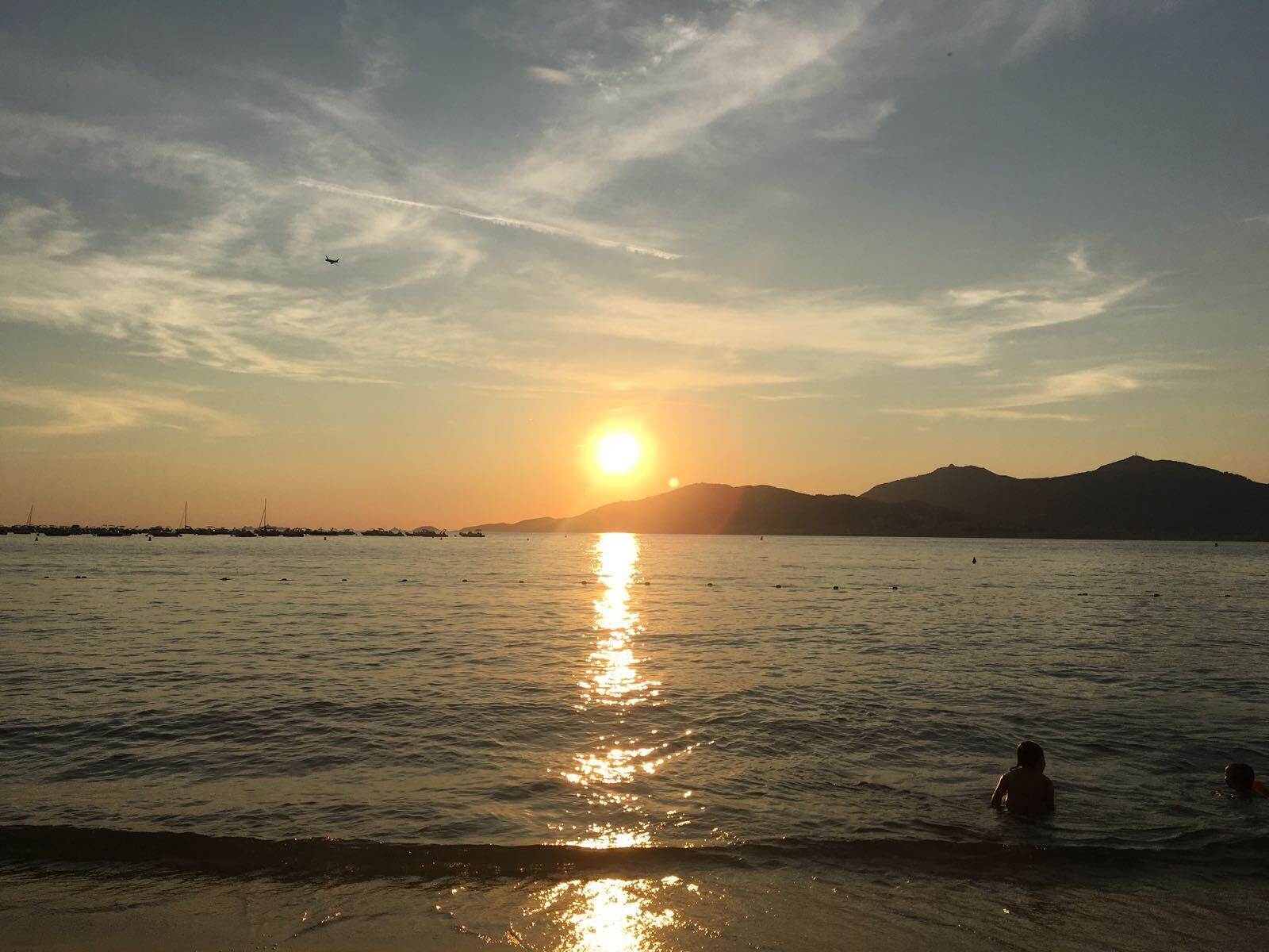 A sunset over a calm sea with boats and a distant mountain range.