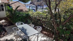 A patio with a table and chairs, surrounded by greenery and overlooking a marina with boats.