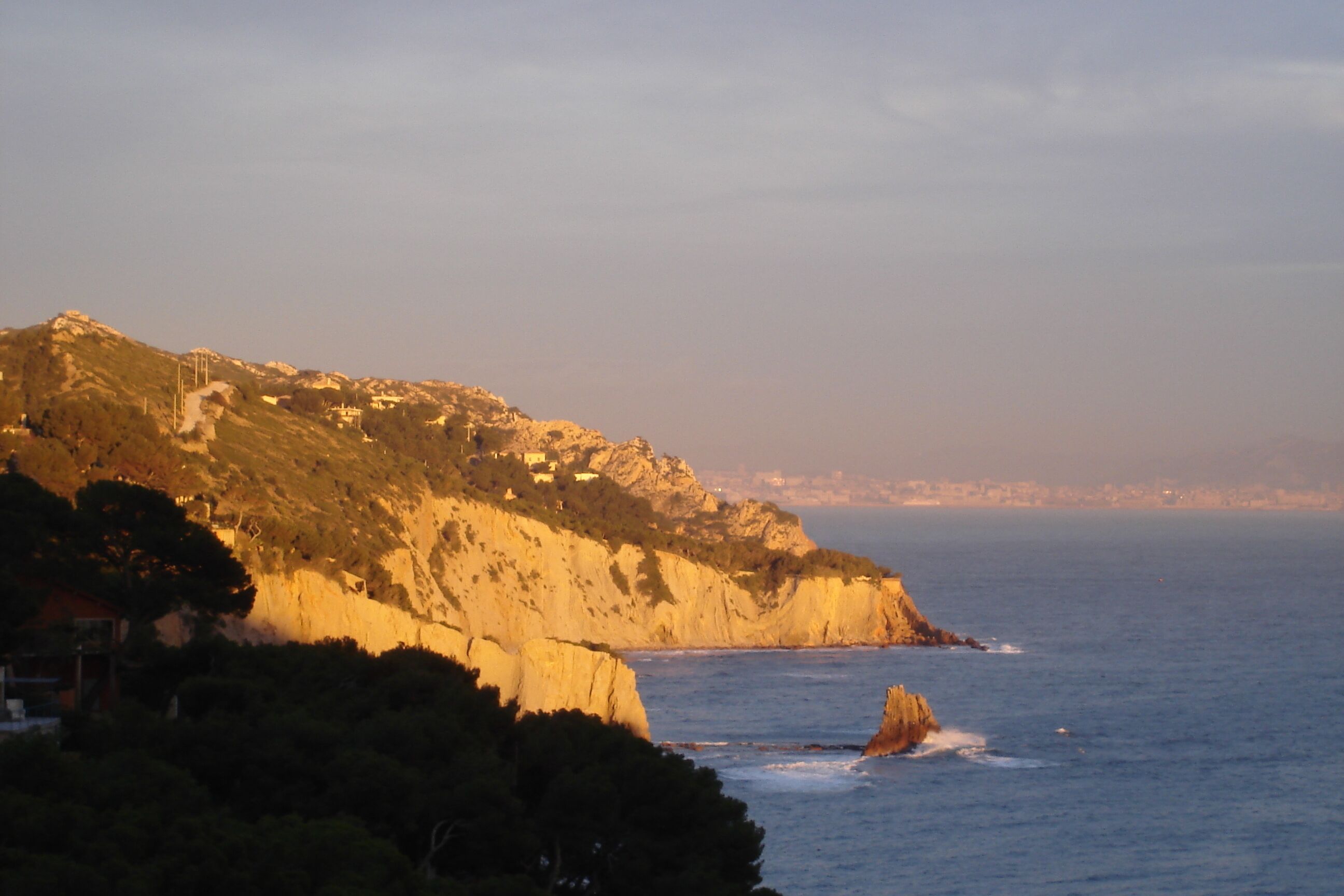 A coastal landscape with a prominent cliff, a small building on the slope, and the sea in the foreground.