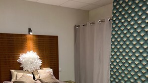 Ein Schlafzimmer mit einem Bett, einem Kopfteil, einer Wand mit Tapete und einem Vorhang.