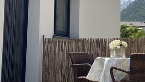 Ein Balkon mit Korbstühlen, einem Tisch und einem Fenster, mit Blick auf Berge.
