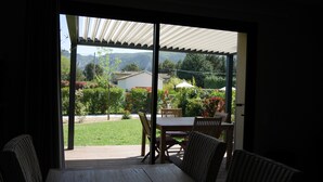 Un patio con mesa y sillas, una zona techada y vistas a un jardín y edificios.