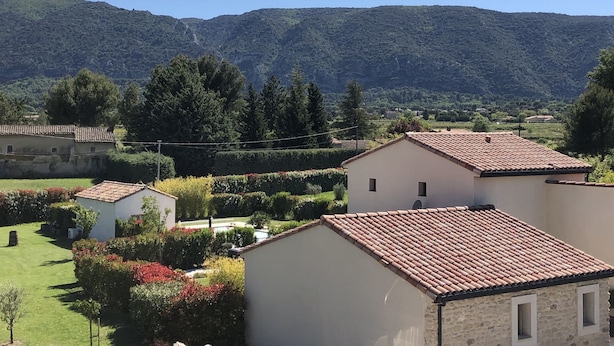 Entorno rural con un edificio blanco de techo rojo, rodeado de vegetación y un telón de fondo montañoso.