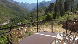 A terrace with a table and chairs, overlooking a mountainous landscape with a river and dense forest. - Weekly and overnight rentals open all year round (Manso)