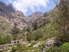 A stone building with a small entrance and windows, surrounded by rocky terrain and sparse vegetation. - Weekly and overnight rentals open all year round (Manso)
