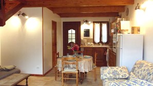 A cozy living room with a wooden ceiling, a dining table with chairs, a sofa, and a kitchen area with a refrigerator and cabinets. - Weekly and overnight rentals open all year round (Manso)