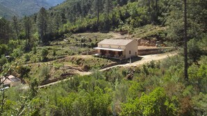 A small, single-story building with a flat roof, surrounded by dense forest and mountains in the background. - Weekly and overnight rentals open all year round (Manso)