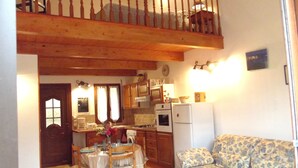 A kitchen with wooden cabinets, a dining table with chairs, a sofa, and a balcony with a railing. - Weekly and overnight rentals open all year round (Manso)