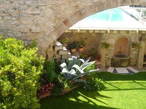 Un arc en pierre mène à un espace piscine agrémenté d’un mur en pierre et de plantes en pot.