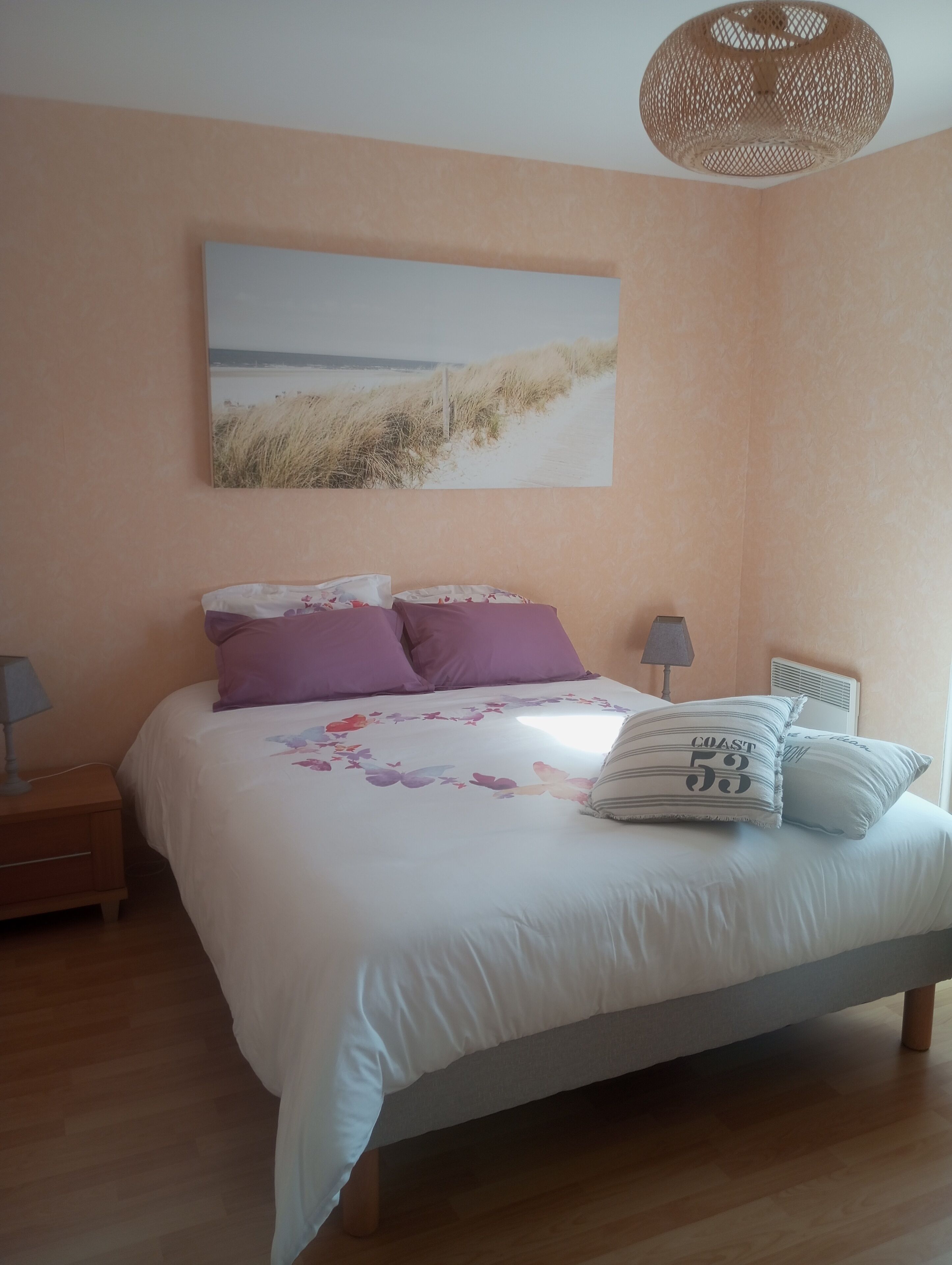 Ein Schlafzimmer mit einem Bett, zwei Nachttischen, einer Wandlampe und einem Gemälde zum Thema Strand.
