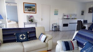 Una sala de estar con un sofá, una mesita de centro con flores y vistas a la cocina.