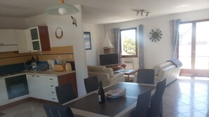 Una cocina moderna con armarios blancos, una mesa de comedor con sillas, un sofá y un televisor.