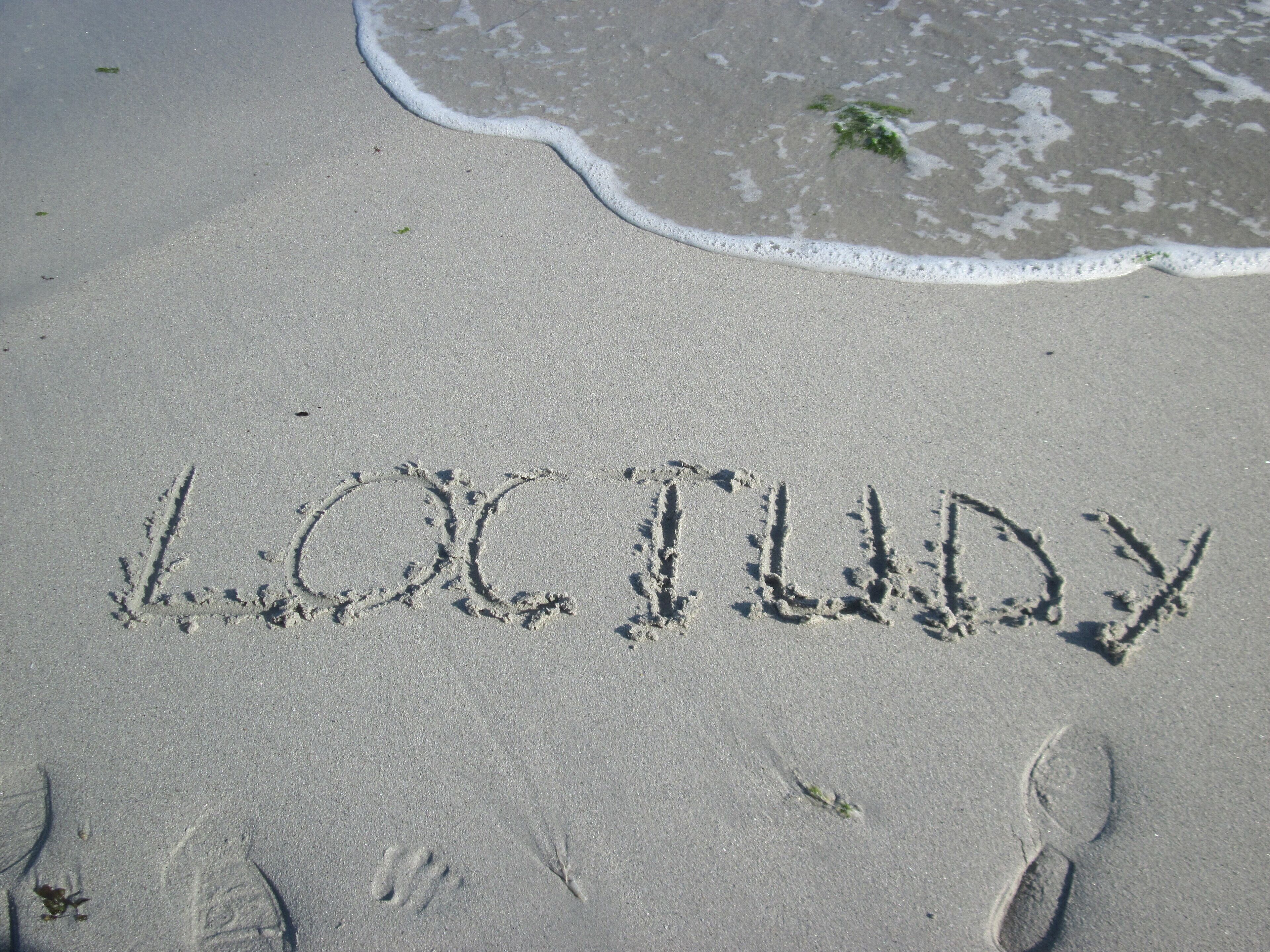 Des empreintes de pas et le mot « LOCTUDY » écrit dans le sable sur une plage.