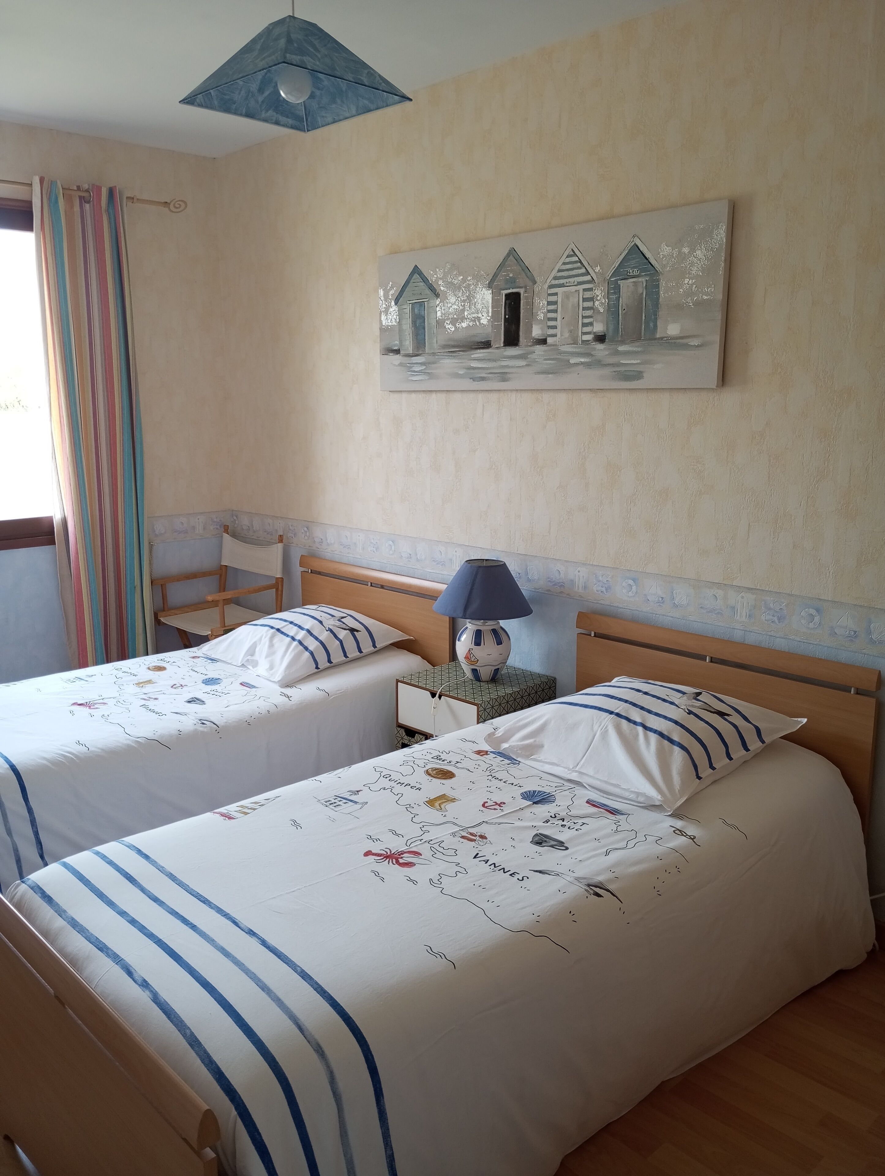 Ein Hotelzimmer mit zwei Betten, einem kleinen Tisch, einer Lampe und einem Bild von Häusern an der Wand.