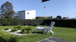 Un patio con una silla de descanso blanca, una mesa y un edificio blanco al fondo.