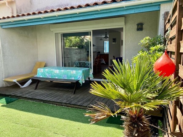 A patio with a table and chairs, a small deck, and a palm plant.