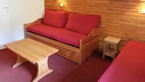 Un sofá de madera con cojines rojos, una mesa de madera y un taburete pequeño en una habitación con paneles de madera.