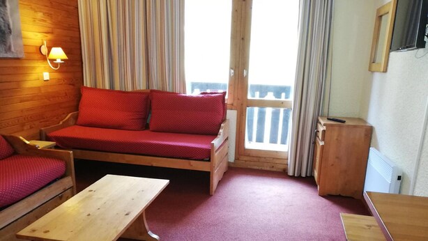Una habitación acogedora con un sofá de madera, dos mesas de madera y vistas al exterior a través de una puerta.
