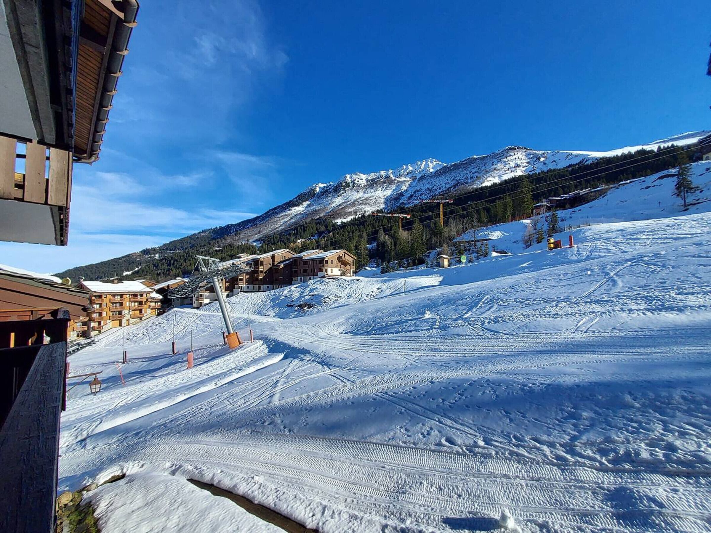 A snow-covered ski slope with buildings and a mountain in the background.