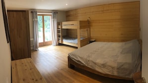 Een slaapkamer met een houten stapelbed, een enkel bed en een schuifdeur naar een balkon.