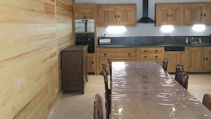 Een keuken met houten kastjes, een grote tafel en een inbouwoven.