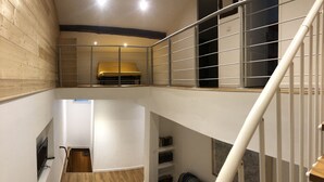 Een meerlaags interieur met een houten vloer, een trap en een geel bed op de bovenverdieping.