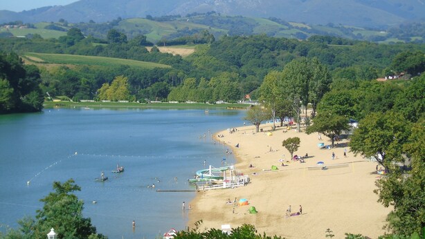 A beach with a mountain in the background, a lake, and a few boats.