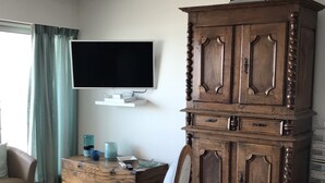 Ein Wohnzimmer mit einem Holzschrank, einem Fernseher auf einem Tisch, einer Couch und einem Sessel.