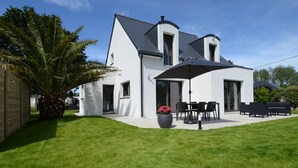 A modern house with a white exterior, a covered patio with outdoor furniture, and a large potted plant.