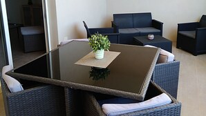 Ein modernes Wohnzimmer mit einem Glastisch, dunklen Korbmöbeln und einem kleinen Topf mit einer Pflanze.