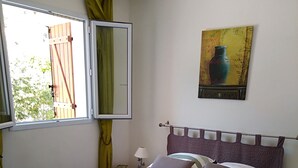 Ein ordentlich bezogenes Bett mit Kopfteil, zwei Nachttische mit Lampen, ein Fenster mit Vorhängen und ein Gemälde an der Wand.