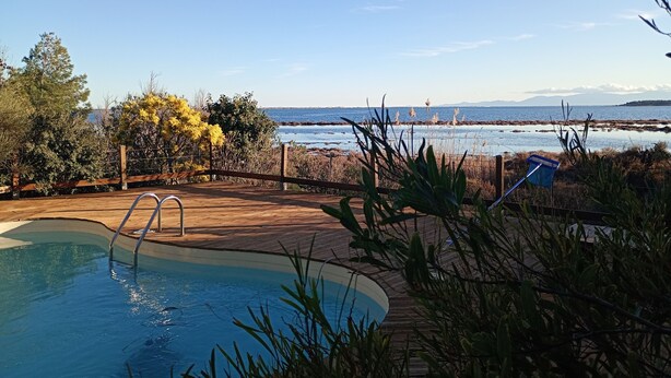A swimming pool with a wooden deck and a view of the ocean.