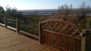 A wooden deck with a metal railing overlooking a coastal landscape with marshy areas and a distant shoreline.