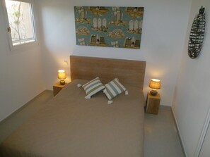 A bedroom with a bed, two bedside lamps, a wall-mounted artwork, and a window.