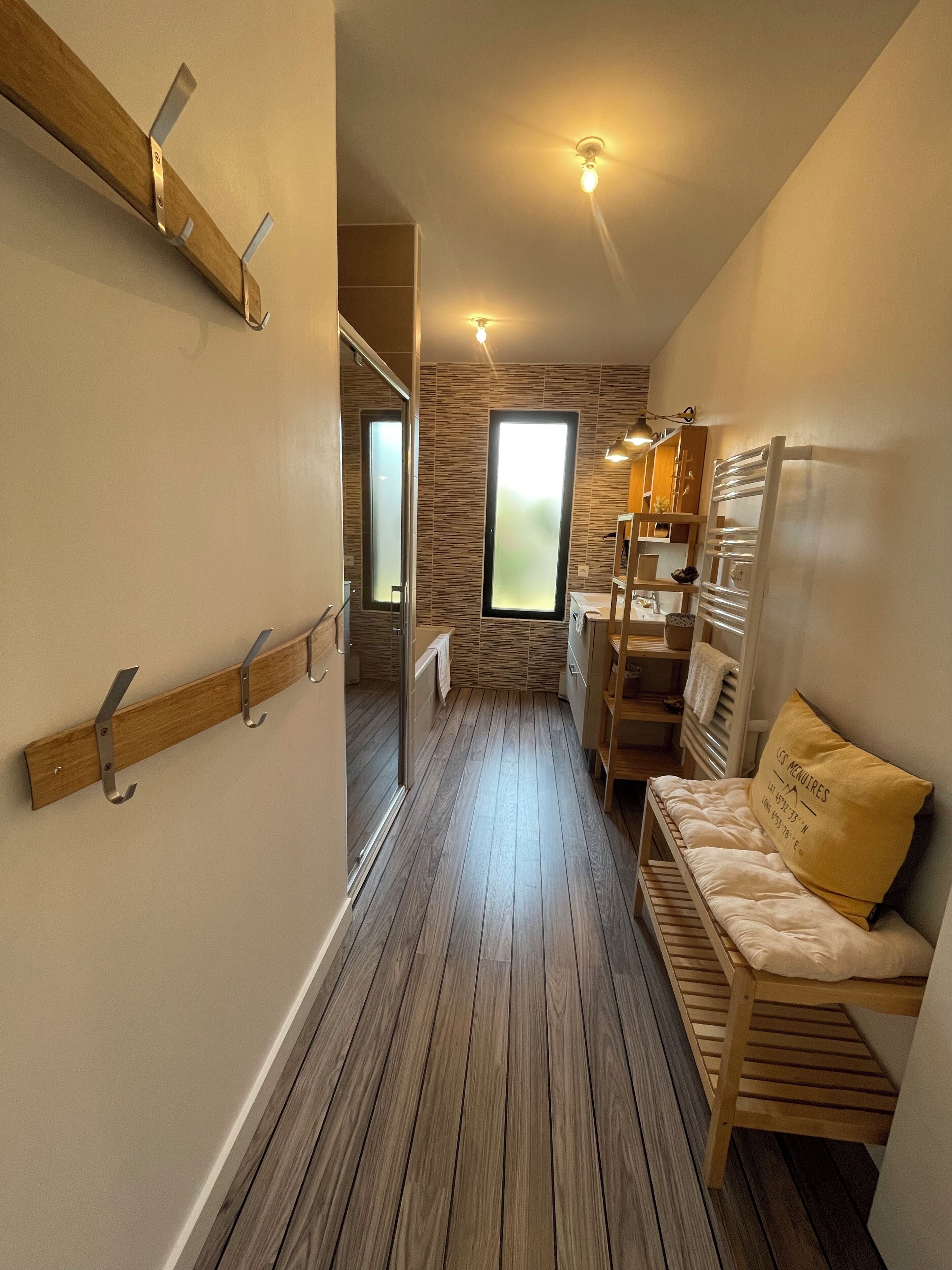 A narrow hallway with wooden flooring, a wooden bench with a cushion, and a window with frosted glass.