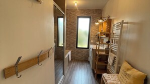 Un pasillo estrecho con suelo de madera, un banco de madera con cojín y una ventana con vidrio esmerilado.