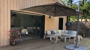 Una terraza de madera con un área de estar techada, una mesa de comedor y un sofá con cojines.