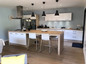 A modern kitchen with white cabinetry, a central island with bar stools, pendant lighting, and a clock on the wall.