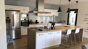 Cocina moderna con electrodomésticos de acero inoxidable, una isla de madera con taburetes altos e iluminación colgante.