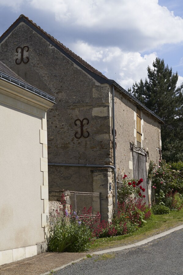 A rustic stone building with a weathered wooden door and a metal gate, surrounded by flowering plants and a clear sky. - L 'Abeille bleue - Cottage *** - 4/6 people - Azay-le-Rideau - from 70 € / night (Cheillé)