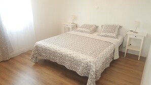 Un dormitorio con una cama, dos mesitas de noche, una lámpara en cada una y un ventanal con cortinas traslúcidas.