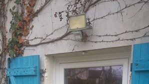 Una puerta blanca con un panel de vidrio, flanqueada por contraventanas de madera azul, y una pequeña placa sobre la puerta.