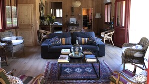 Una sala de estar acogedora con un sofá, sillones y una mesa de centro. Hay libros y una lámpara sobre la mesa.